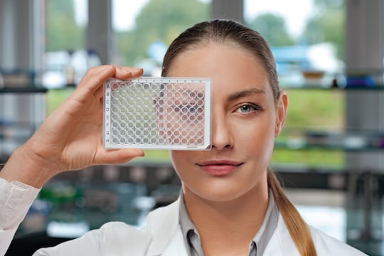 Woman in lab coat looking through microplate