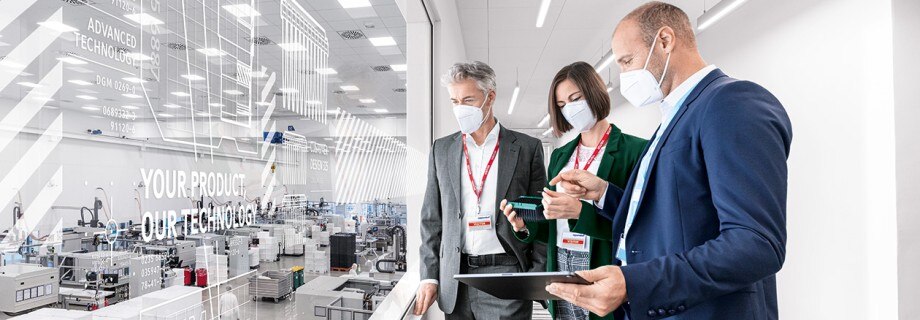 IVD-Ready Customized Solutions with Eppendorf OEM. With mask, three people watching production facilities through window, focus on tray with black OEM tips as customized solution.