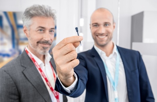 OEM partnership at eye level. Two men holding a black OEM pipette tip as customized solution with toolshop in the background.