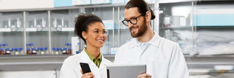 Improve your daily lab routines with lab management software Two people in the laboratory monitoring their digital lab activity from a tablet and smartphone
